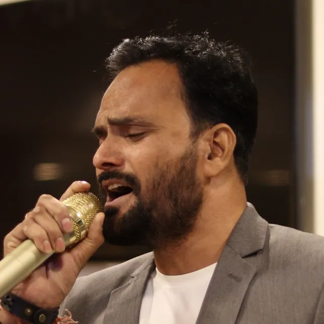 Man in a gray blazer singing into a gold vintage-style microphone