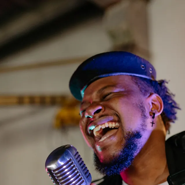 Man in a cap laughing as he sings into a chrome vintage microphone