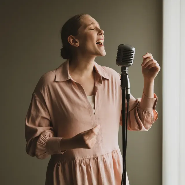 Soprano in a soft pink blouse singing with her eyes closed into a vintage microphone