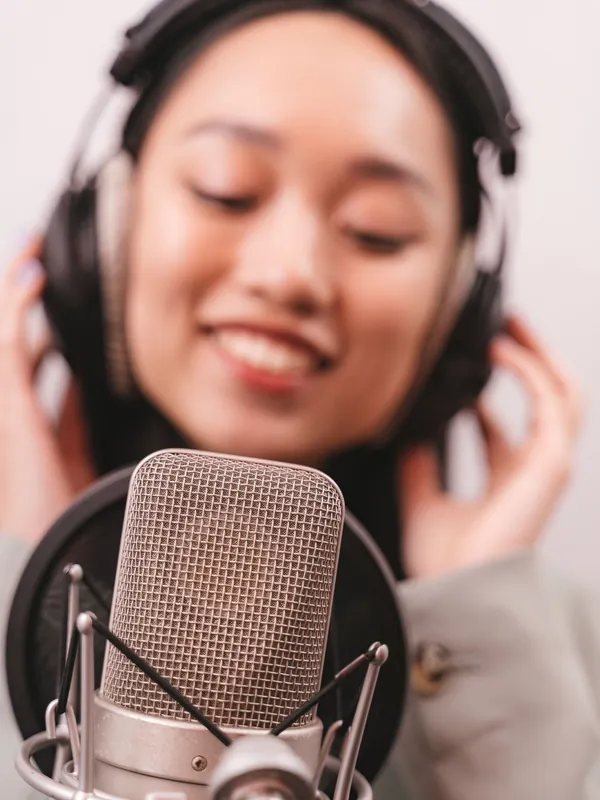 Smiling woman in headphones singing softly into a studio microphone