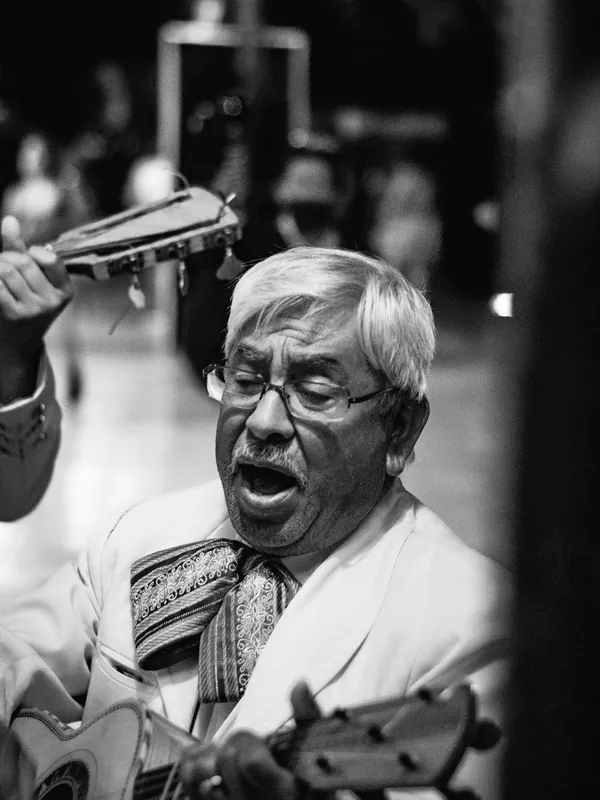 Older man with glasses singing with gusto, in a black-and-white street photo