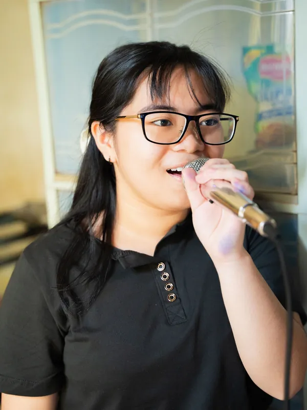 Young woman with glasses singing karaoke into a handheld microphone