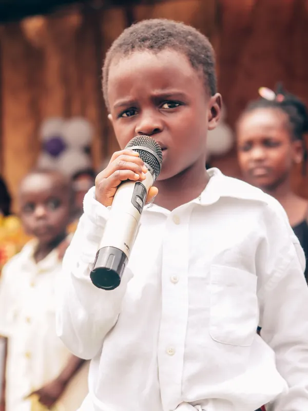 Boy in a white shirt singing into a microphone at an outdoor event